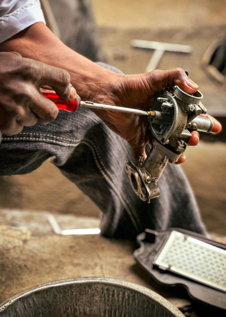 Detailed image of a mechanic using a screwdriver to repair a carburetor, showcasing hands-on work.